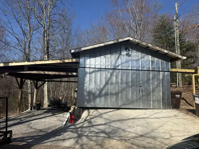 Metal storage building with an attached carport on a concrete pad in a wooded yard