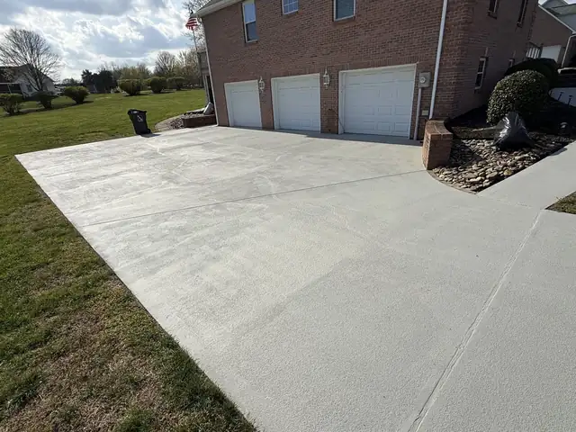 Wide new concrete driveway extension beside a brick home with three garage doors